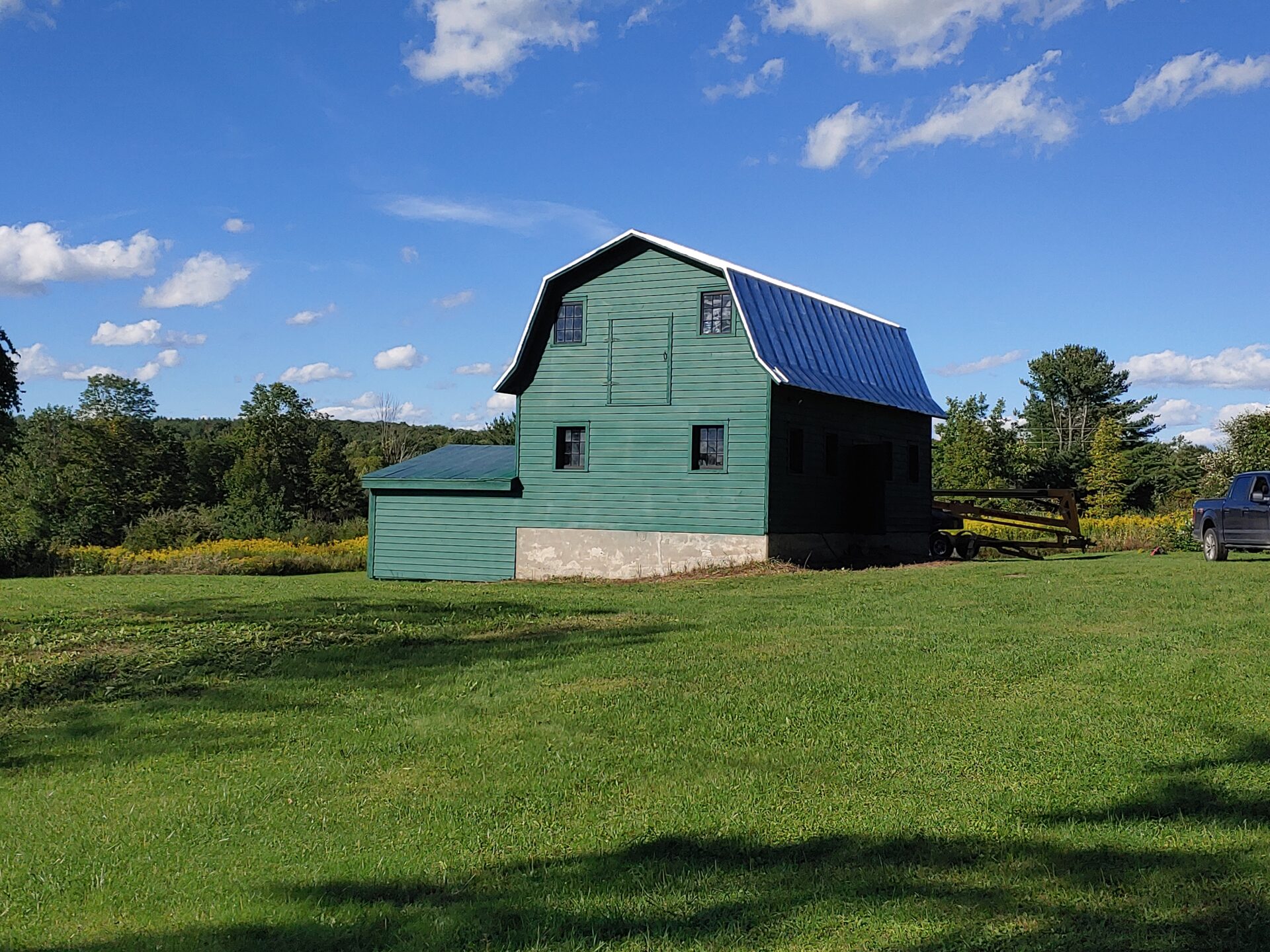 A green barn sitting in the middle of a field.