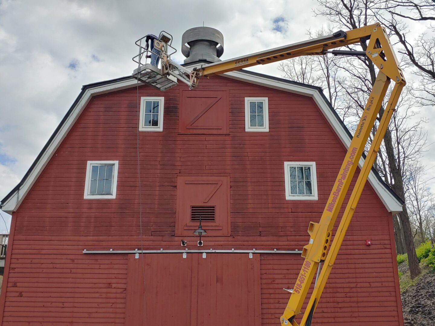A red barn with a man on a crane