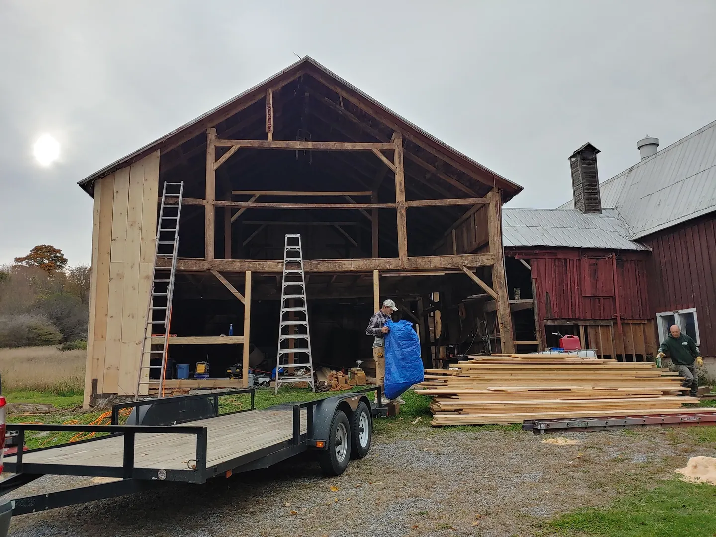 A man standing next to a trailer in front of a barn.